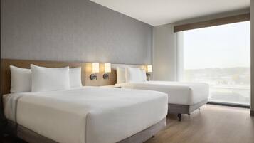 A hotel room with a large bed, two bedside tables with lamps, a window with a city view, and a wooden floor.