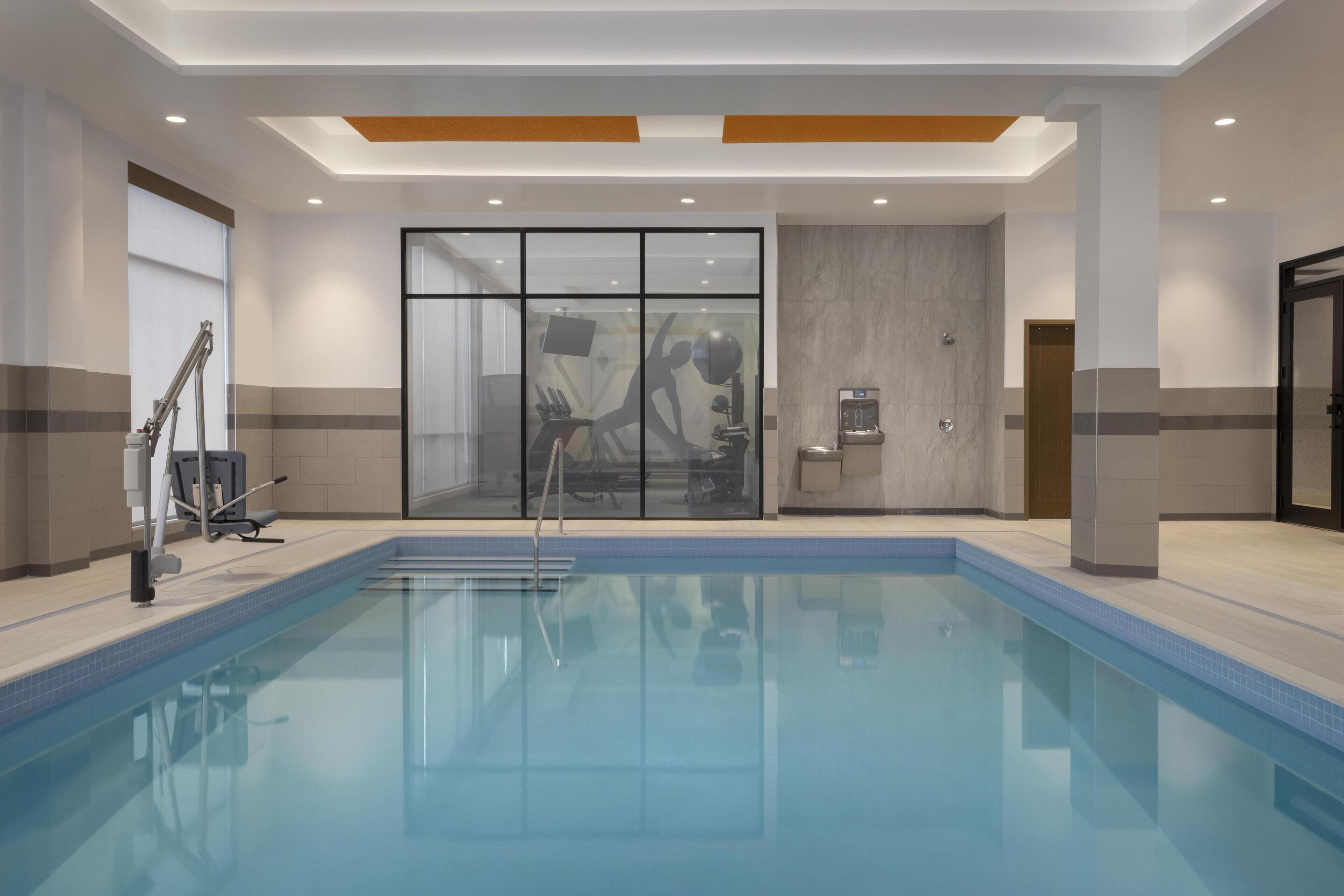 Ein Schwimmbad mit Glaswand, einer Springbrunnenanlage und Fitnessgeräten.