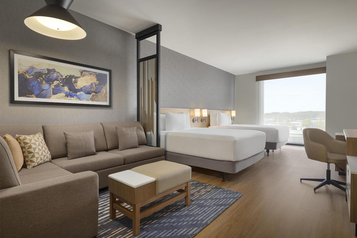 Ein modernes Hotelzimmer mit Sofa, Bett, Schreibtisch und großem Fenster mit Blick auf die Stadt.
