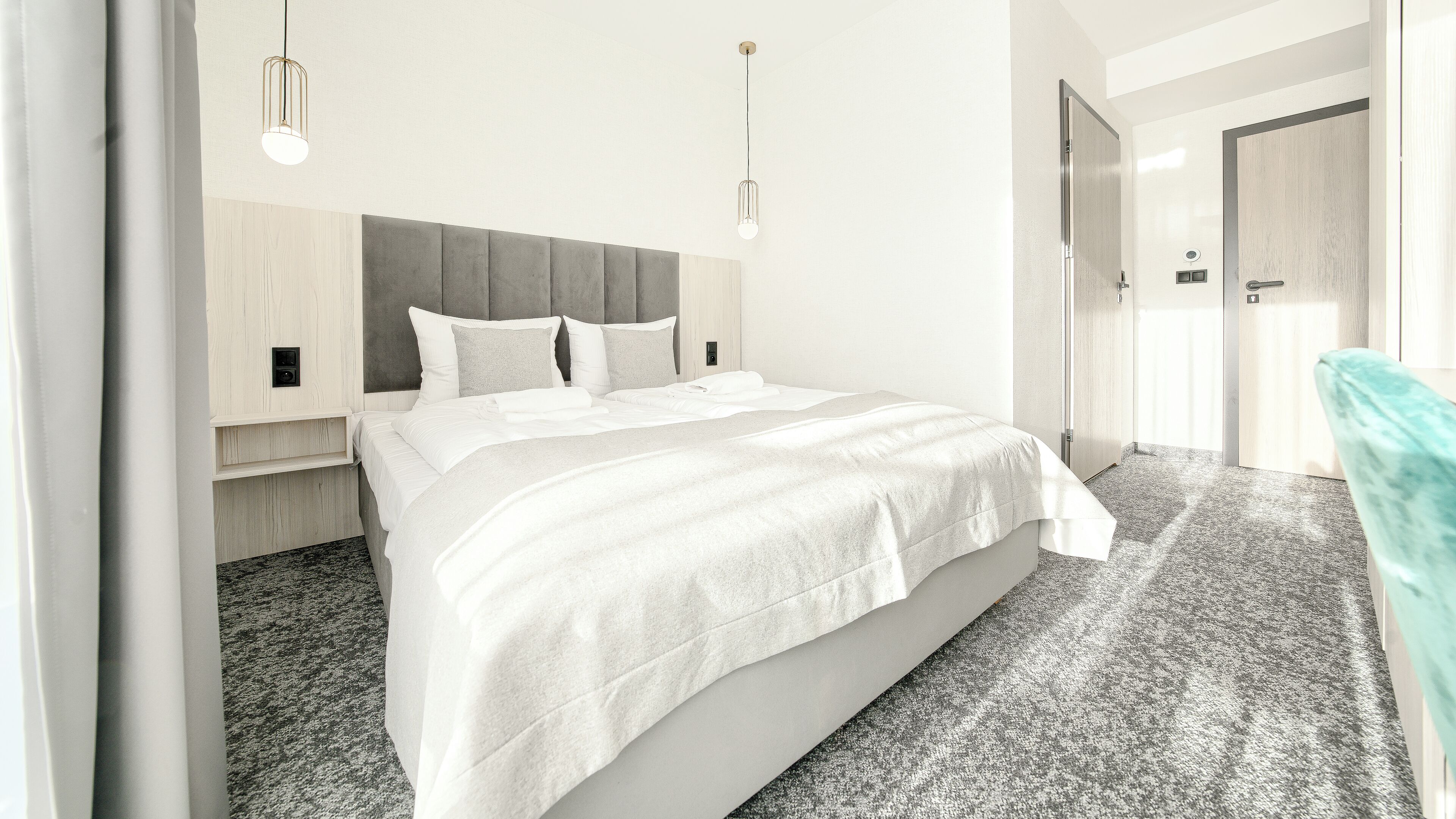 Una habitación de hotel moderna con una cama grande, cabecera gris y alfombra de color claro.