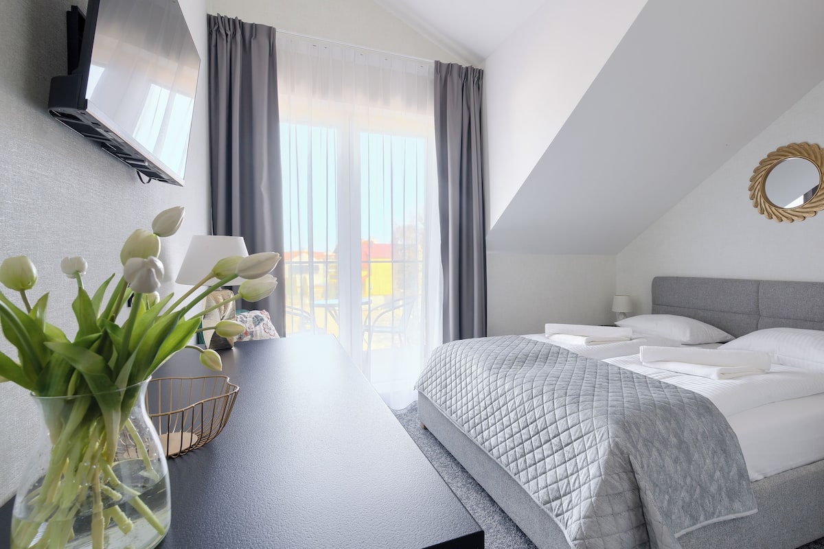 A modern bedroom with a bed, a desk, and a view of the outdoors.