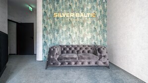 A grey upholstered sofa in a hallway with a textured wall and a sign reading "SILVER BALTIC APARTMENTS". - Apartamenty Sun & Snow Na Spokojnej (Kolobrzeg)