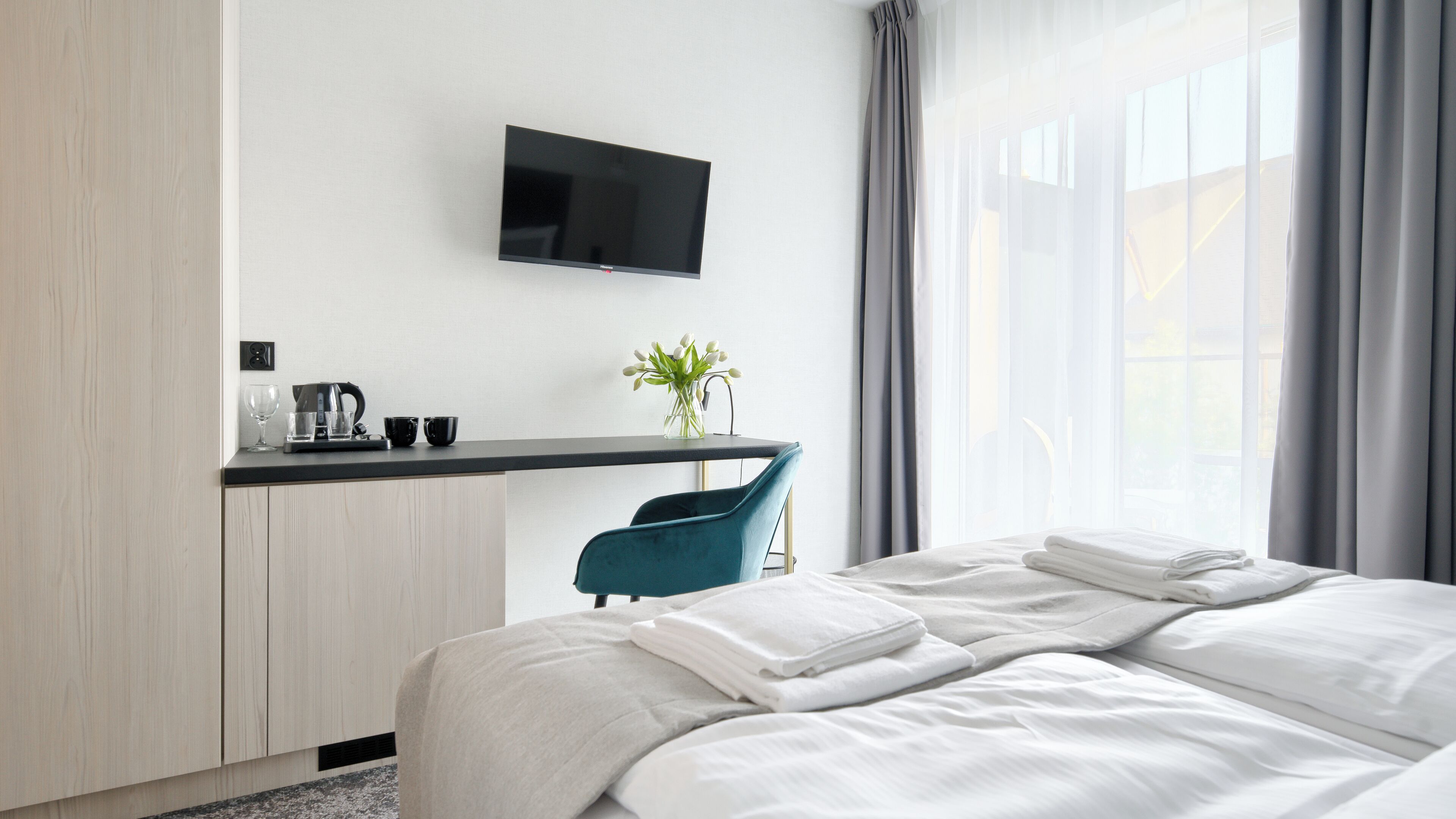 Una camera d'albergo con un letto, una scrivania con televisione a schermo piatto, una sedia e una finestra con tende.