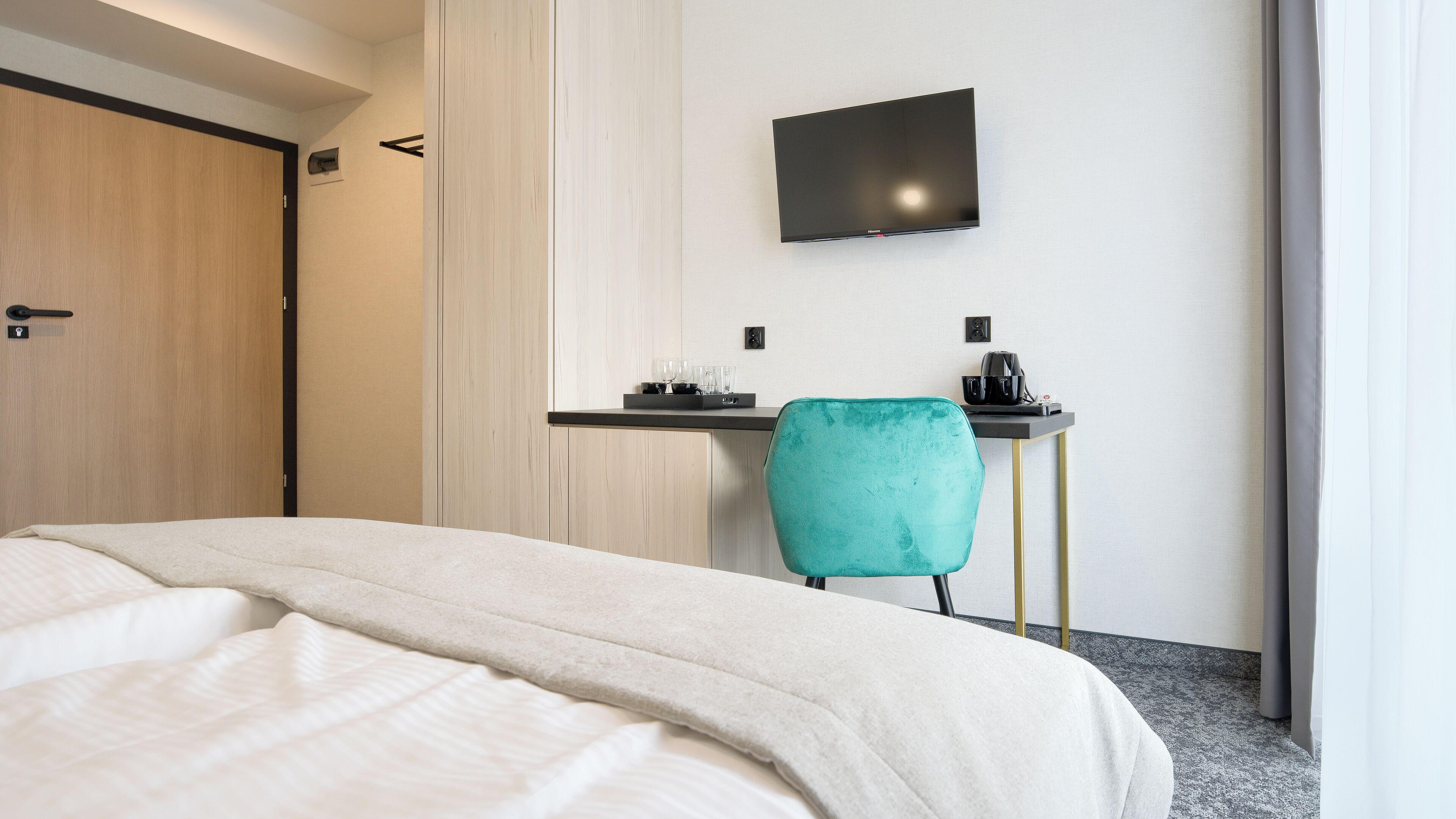 A hotel room with a bed, a desk with a chair, a flat-screen TV, and a coffee machine.