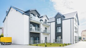 A modern multi-story building with balconies, a covered parking area, and a clear sky. - Apartamenty Sun & Snow Na Spokojnej (Kolobrzeg)