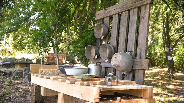 Un entorno rústico al aire libre con un banco de madera y diversos utensilios y recipientes de cocina.