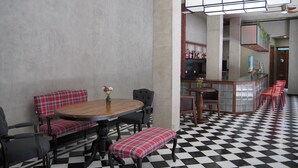 A dining area with a checkered floor, a round wooden table, and red plaid upholstered seating. - Station22 (Batumi)