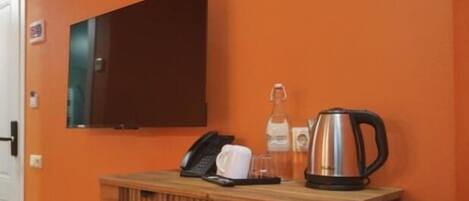 A room with an orange wall, a wooden table with a telephone, a coffee pot, and a small stool.
