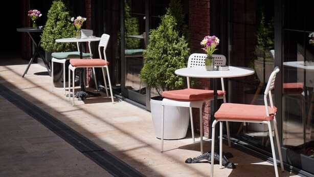 An outdoor seating area with tables and chairs, potted plants, and a brick wall. - Station22 (Batumi)