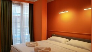 A hotel room with a large bed, two pillows, a bedside table, and a window with curtains. - Station22 (Batumi)