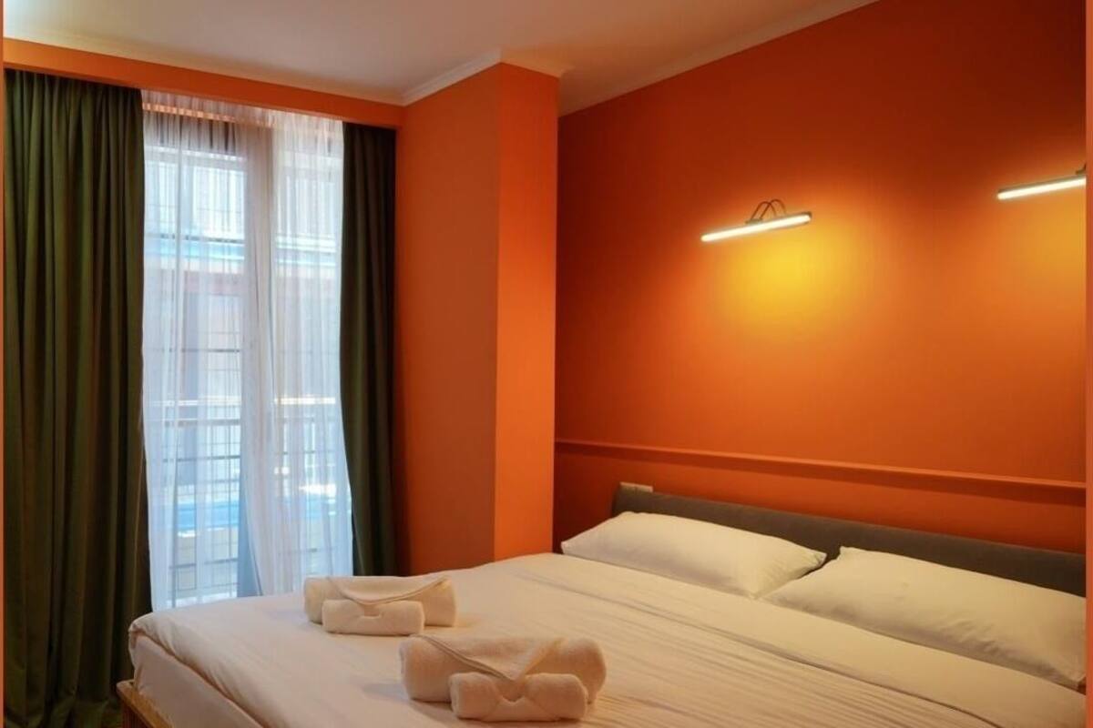 A hotel room with a large bed, two pillows, a bedside table, and a window with curtains.