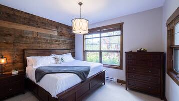 Une chambre à coucher avec une tête de lit en bois, une grande fenêtre, une commode et un luminaire suspendu.