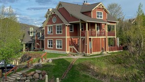 A large, two-story house with a red exterior, multiple windows, and a balcony on the second floor.