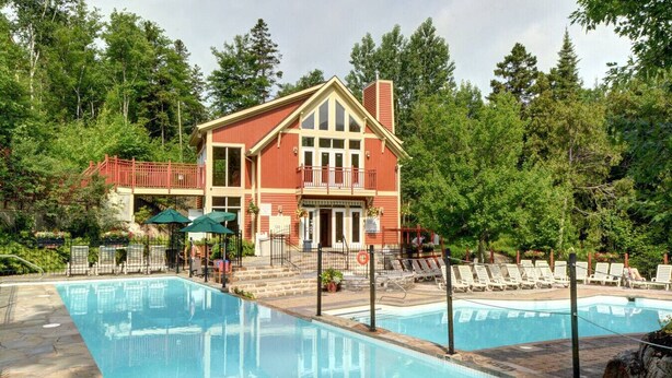 A two-story building with a pool, surrounded by trees.