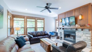 A modern living room with a stone fireplace, leather sofas, and a flat-screen TV mounted above it.