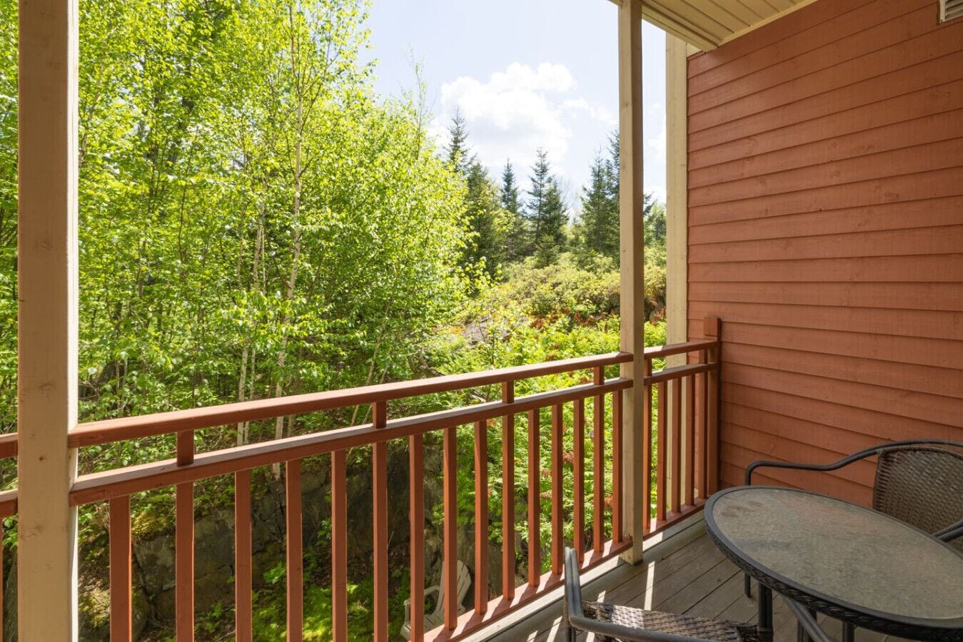 Un balcon en bois, doté d’une rambarde en métal, qui donne sur une zone boisée.