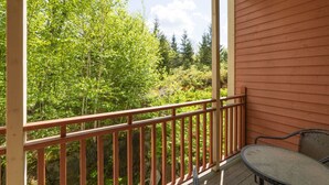 A wooden balcony with a metal railing overlooking a forested area.
