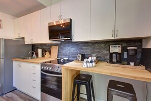 A modern kitchen with white cabinets, a stainless steel oven, a microwave, and a coffee maker. - Cozy Lodge in the Mont Tremblant Ski Village (Mont-Tremblant)