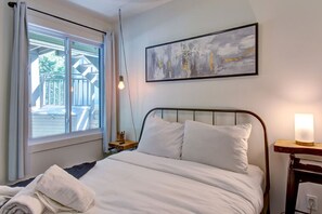 A bedroom with a bed, a window with a view of a deck, a painting on the wall, and a bedside lamp. - Cozy Lodge in the Mont Tremblant Ski Village (Mont-Tremblant)