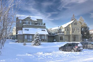 A two-story house with a balcony, surrounded by snow-covered ground and trees.