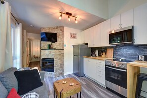 A modern kitchen with a stone fireplace, a built-in oven, and a dining area with a small table and sofa. - Cozy Lodge in the Mont Tremblant Ski Village (Mont-Tremblant)