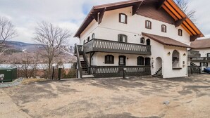 A two-story building with a balcony, a staircase, and a view of mountains in the background. - Bright & Modern Lac Tremblant Condo + Views (Mont-Tremblant)