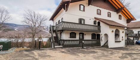 Ein zweistöckiges Gebäude mit Balkon, Treppe und Bergblick im Hintergrund.