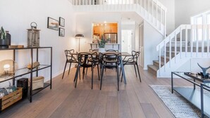 A spacious living area with a dining table and chairs, a staircase, and a kitchen in the background. - Bright & Modern Lac Tremblant Condo + Views (Mont-Tremblant)