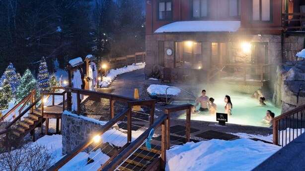 A wooden lodge with a hot spring area, wooden deck, and snow-covered surroundings.