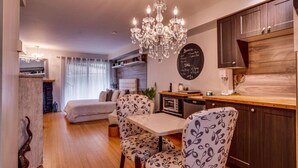 A cozy living room with a dining area, a chandelier, and a kitchen with a chalkboard menu.