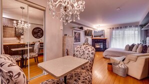 A cozy living room with a fireplace, a dining area with a chandelier, and a bedroom with a large bed and a nightstand.