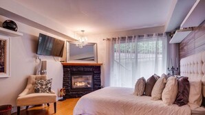 A bedroom with a large bed, a fireplace, a television, and a chair.