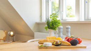 En köksbänk med ett bröd, en ost, en tomat, en avokado, en pepparkvarn och en vas med örter.