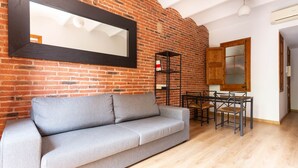 A living room with a grey sofa, a wooden dining table with chairs, a black metal shelf, and a large mirror on a brick wall. - Amazing Classic Apartment by Sagrada Familia With Balcony an (Barcelona)
