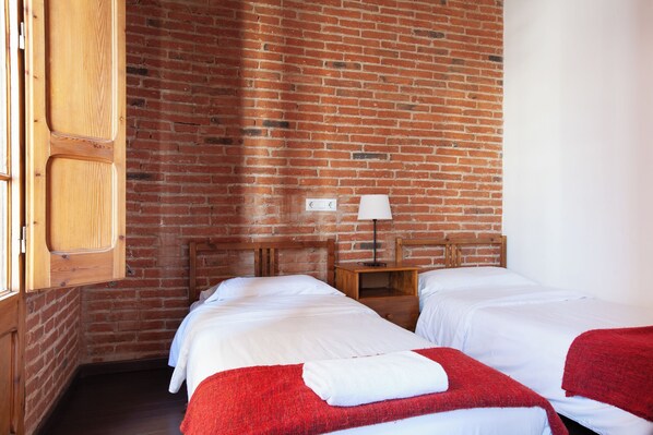 Una habitación con dos camas, un cabecero de madera, una mesita de noche con lámpara y una pared de ladrillo.