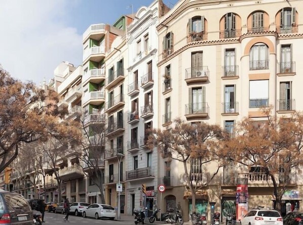 A multi-story building with balconies, a 3D parking sign, and parked cars on the street.