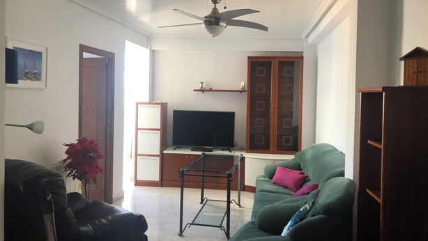 A living room with a ceiling fan, a television, a green sofa, a black leather chair, and a wooden cabinet. - Almería Centro (Almería)