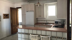 A kitchen with a refrigerator, microwave, sink, and two white chairs. - Almería Centro (Almería)