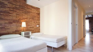 A modern bedroom with a brick accent wall, two beds, a bedside table with a lamp, and a wooden floor. - 2-bedroom Apartment in the Old Town (Barcelona)