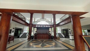 Un vestíbulo amplio con un mostrador de recepción central, un suelo con diseño y una escalera que sube a un nivel superior.