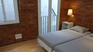 Une chambre avec deux lits, un mur en briques, une fenêtre et une table de chevet avec une lampe.