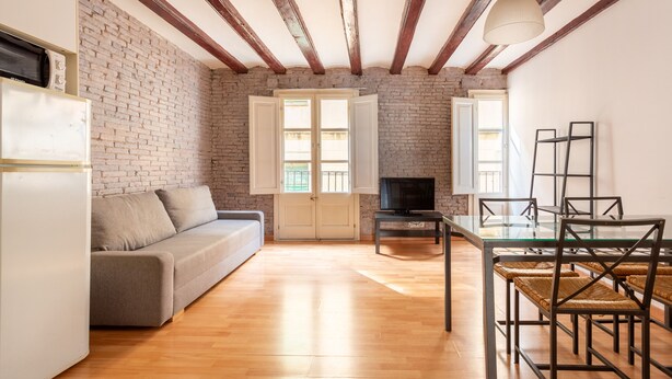 Ein Wohnzimmer mit einer Couch, einem Fernseher, einem Glastisch und Korbstühlen.