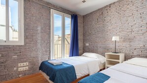 Ein Zimmer mit zwei Betten, einer Ziegelwand, einem Fenster mit Vorhängen und einem Nachttisch mit Lampe.