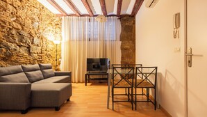 A living room with a stone wall, a sofa, a TV, and a dining table with chairs. - Apartment near Ramblas for families or friends (Barcelona)