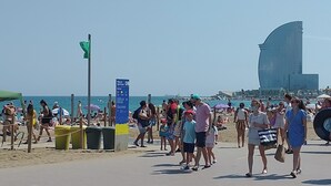 A crowded beach with people walking, umbrellas, and a large building in the background. - Lovely flat in Barceloneta near sea (Barcelona)