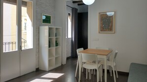 A dining area with a wooden table and white chairs, a white shelving unit, and a hanging light fixture. - Lovely flat in Barceloneta near sea (Barcelona)