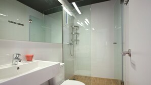 Casa de banho moderna com chuveiro separado por vidro, pia branca e sanita.