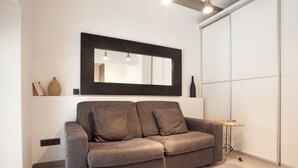 Uma sala de estar moderna com um sofá cinzento, um espelho grande e uma pequena mesa lateral.