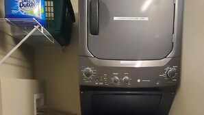 Une machine à laver compacte, de couleur sombre, se trouve dans une petite pièce dont le sol est recouvert de parquet.