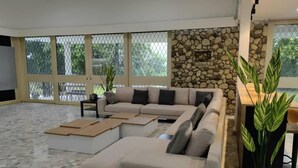 Un salón amplio con un sofá seccional en forma de L, una chimenea de piedra y ventanas grandes con vistas a la vegetación.